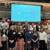 Large group of students, faculty and donors stand in a group in a gym, smiling for a photo